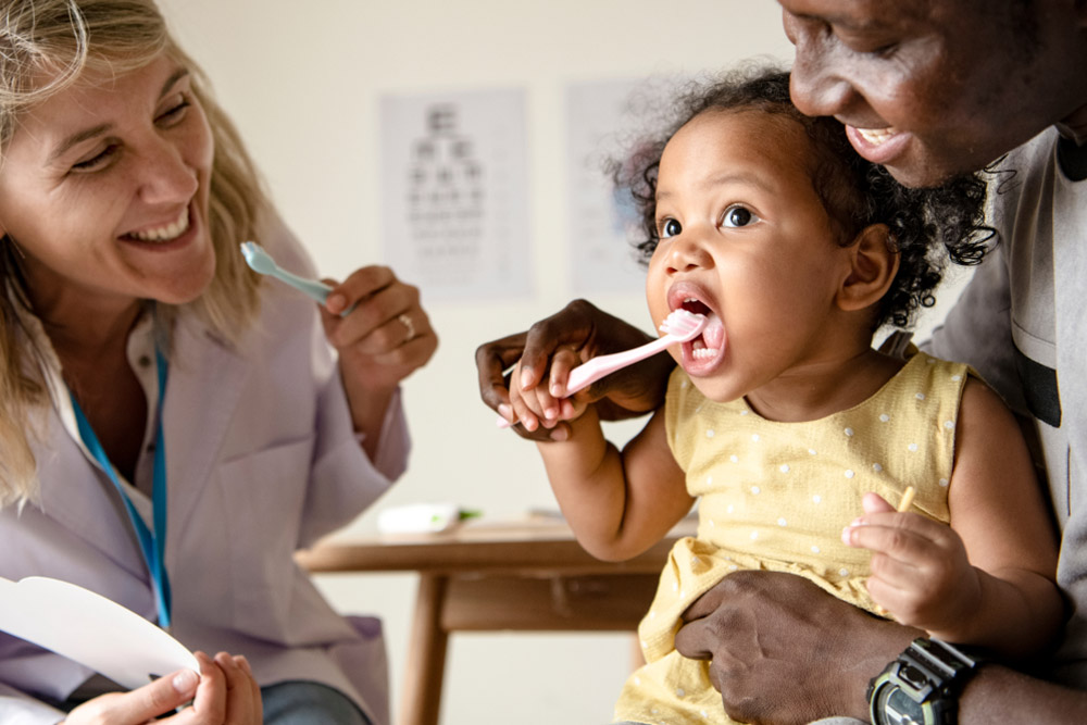 Dentist teaching a little girl how to brush her teeth