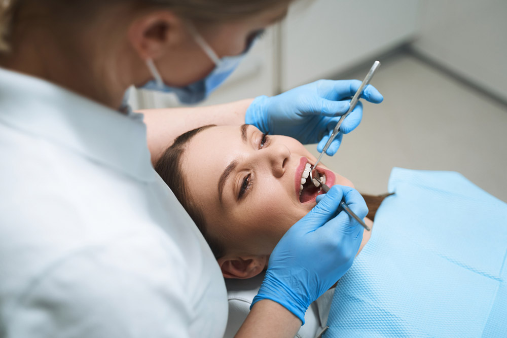 Young lady is lying in dental chair while female doctor is using instruments for examination